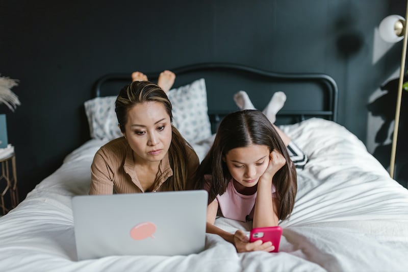 mujeres con su celular y computadora en la cama