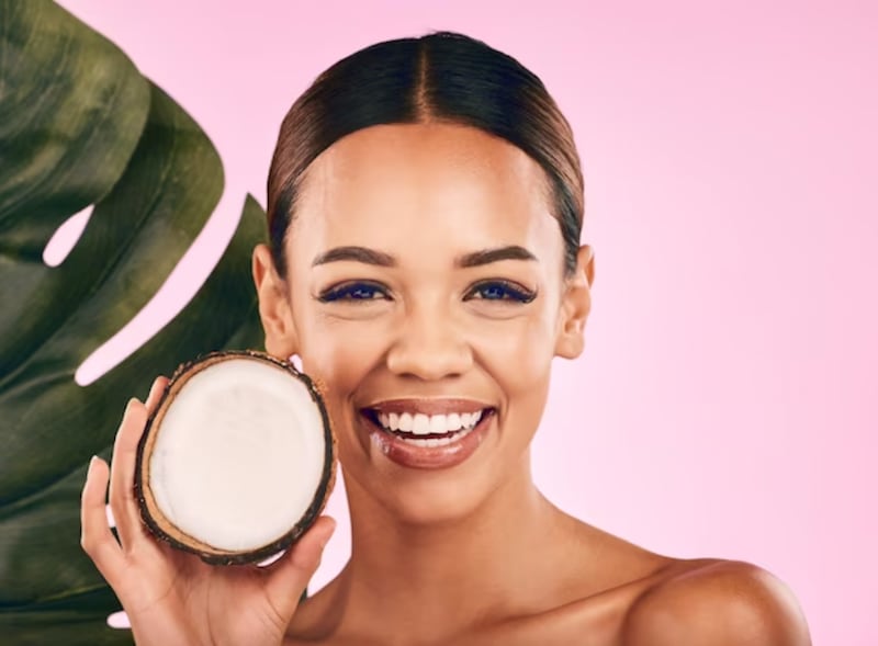 Mujer con un coco en la mano con fondo rosa.